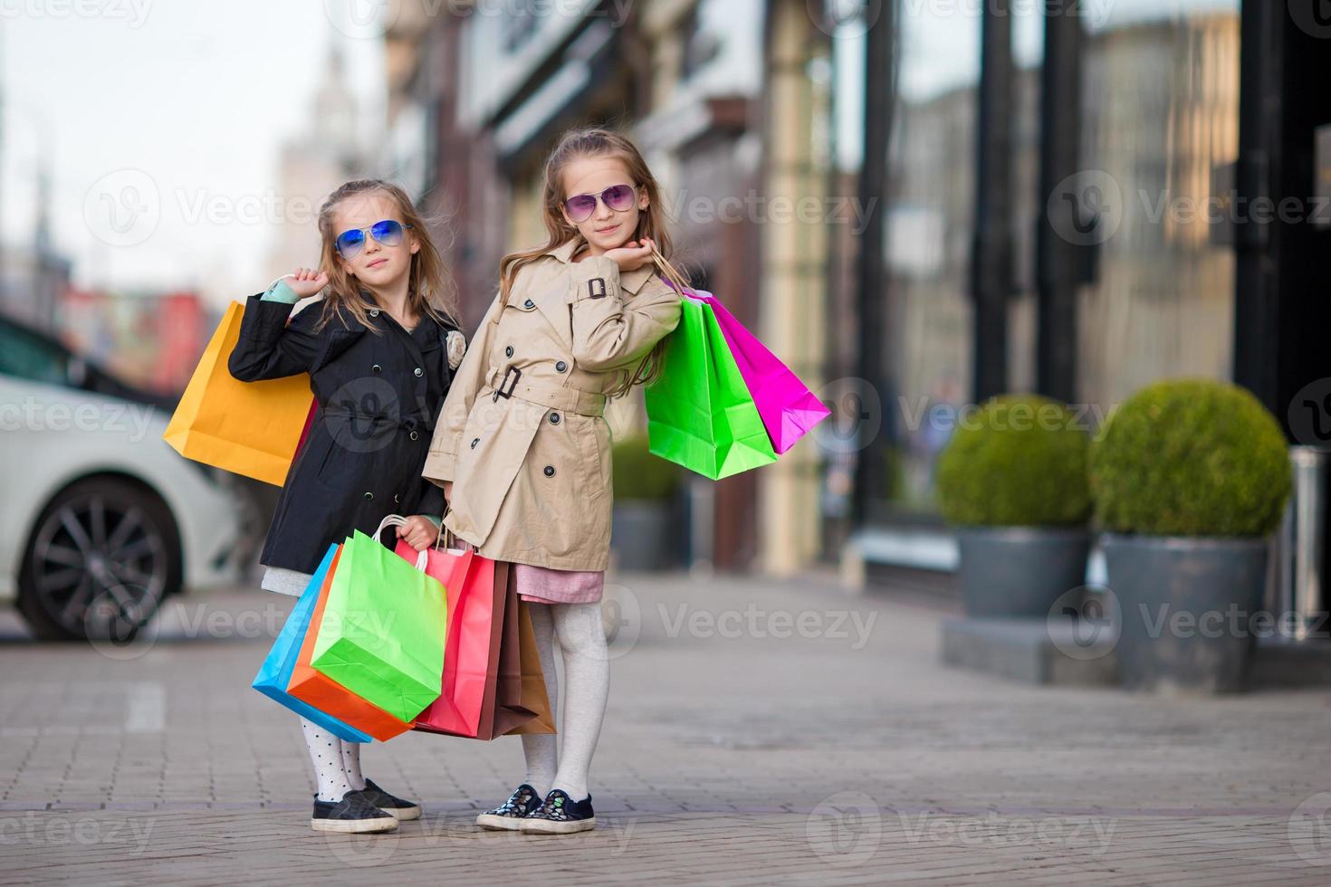 aanbiddelijk weinig meisjes met Tassen Aan boodschappen doen buitenshuis foto