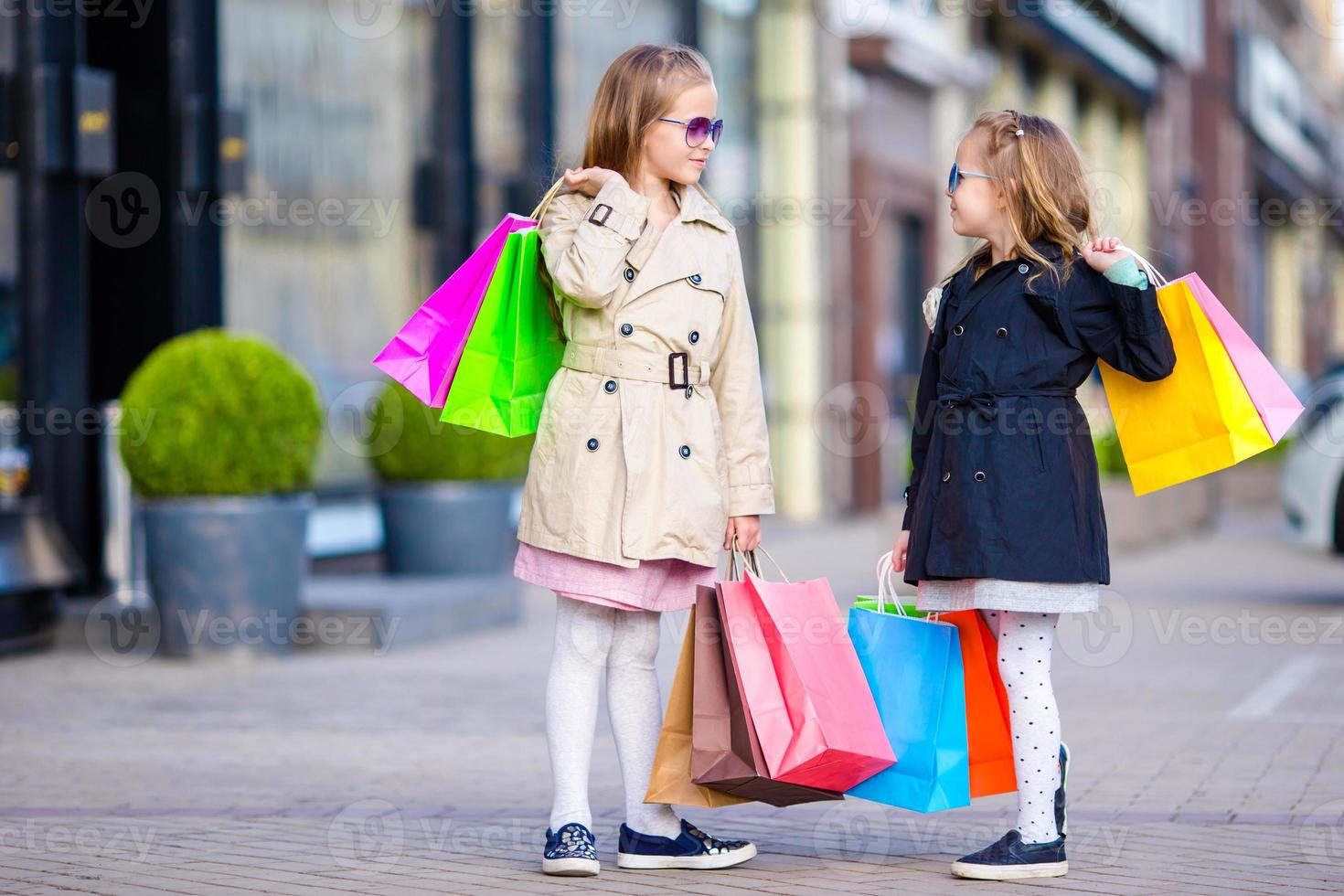 aanbiddelijk weinig meisjes Aan winkelen. portret van kinderen met boodschappen doen Tassen. foto