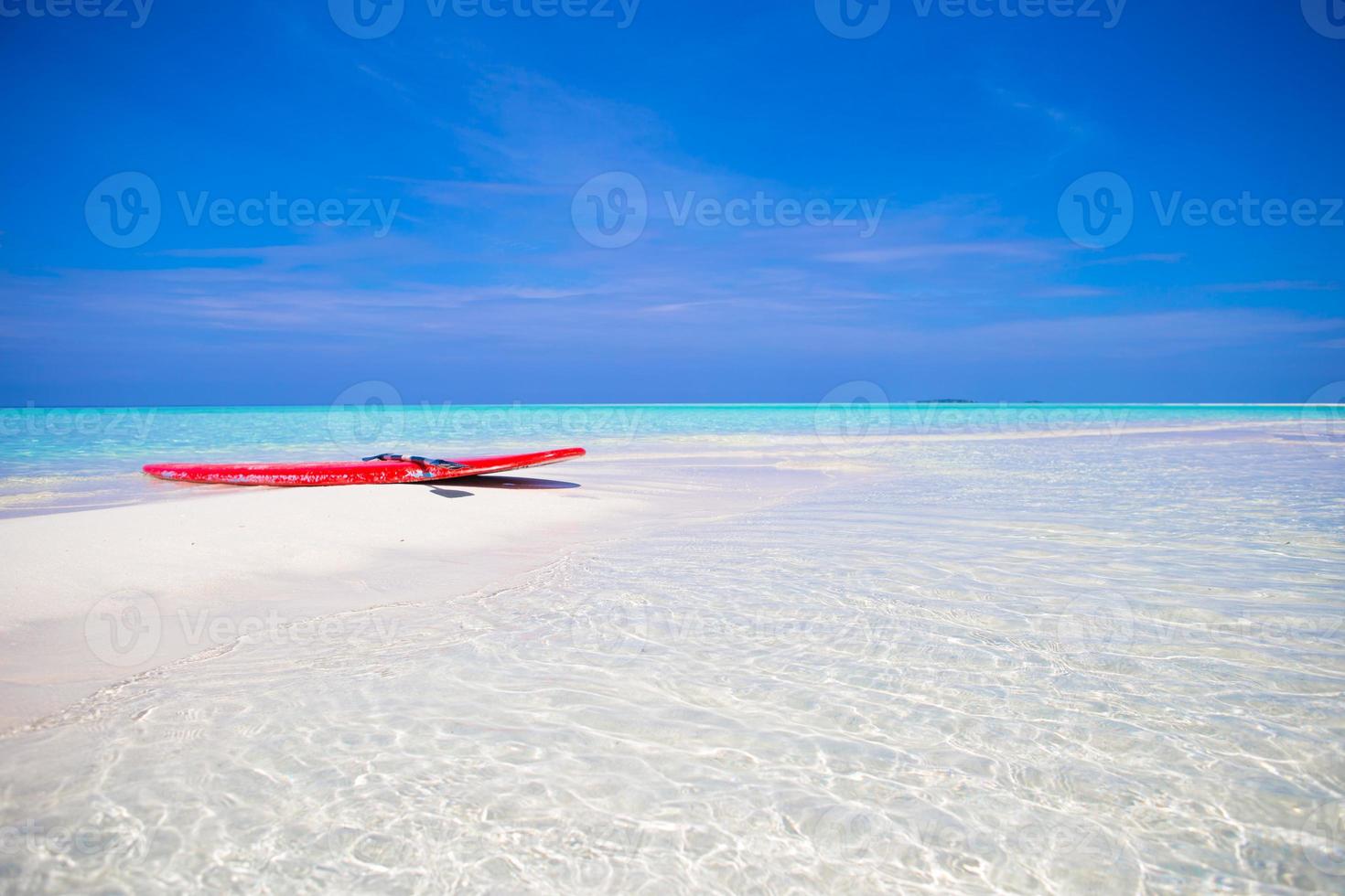 rood surfboard Aan wit zanderig strand met turkoois water Bij tropisch eiland in Indisch oceaan foto