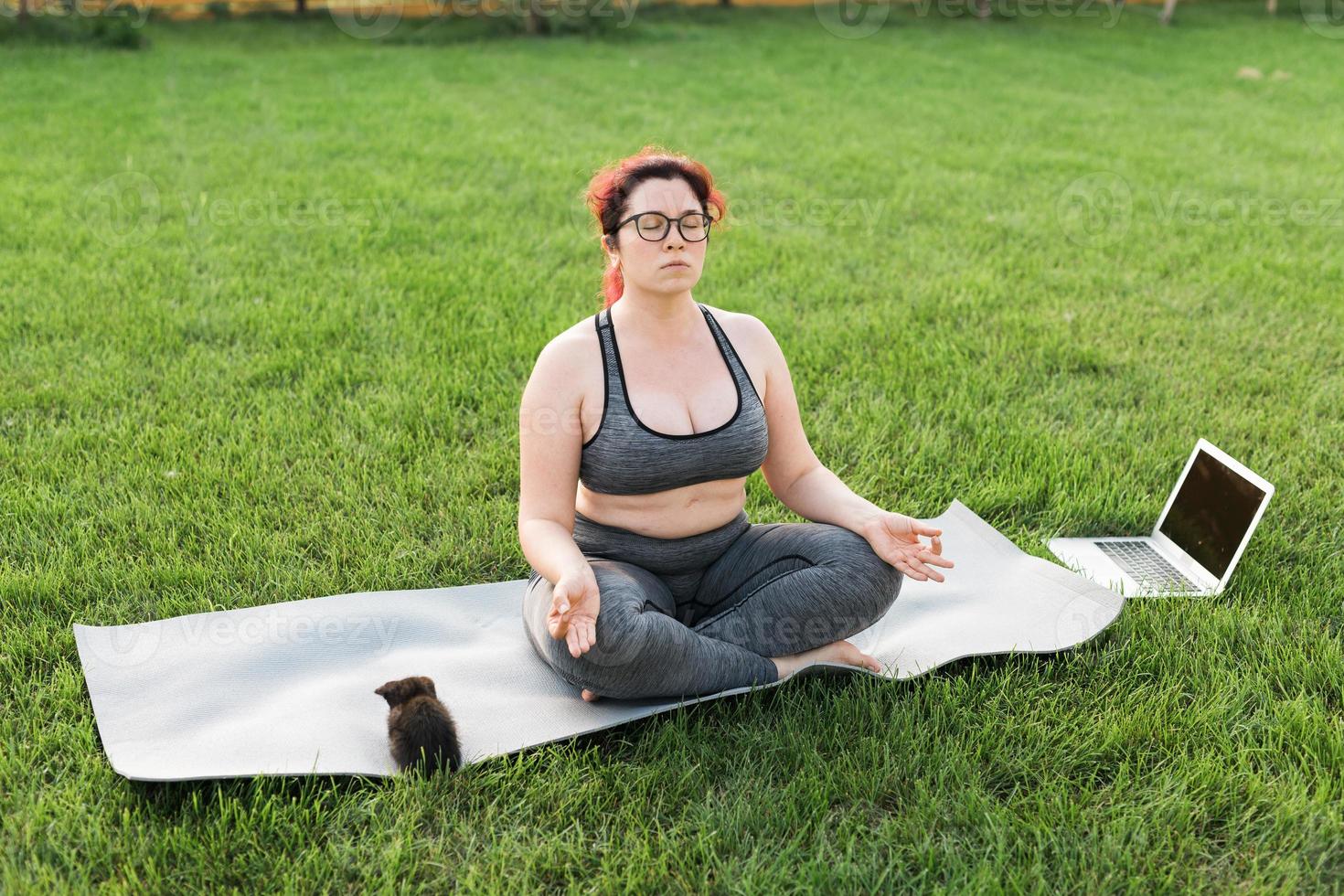 plus grootte lichaam positiviteit vrouw aan het doen meditatie Aan yoga mat met katje Aan achtertuin - welzijn en mentaal Gezondheid concept foto