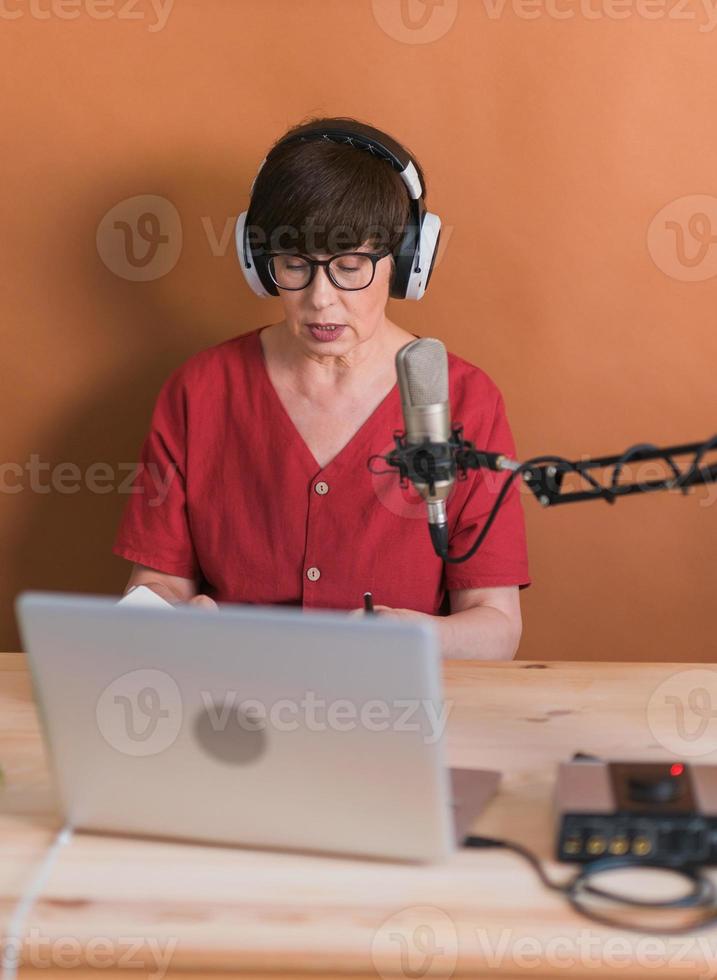 middelbare leeftijd vrouw radio presentator pratend in de microfoon en lezing nieuws - radio uitzending online concept foto