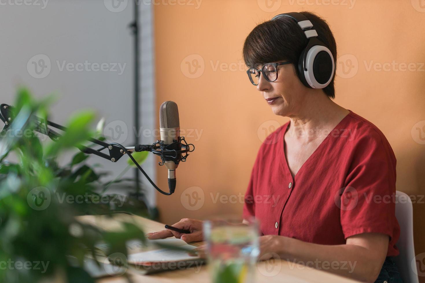 volwassen vrouw maken podcast opname voor haar online show. aantrekkelijk bedrijf vrouw gebruik makend van hoofdtelefoons voorkant van microfoon voor een radio uitzending foto