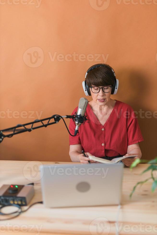 middelbare leeftijd vrouw radio presentator pratend in de microfoon en lezing nieuws - radio uitzending online concept foto