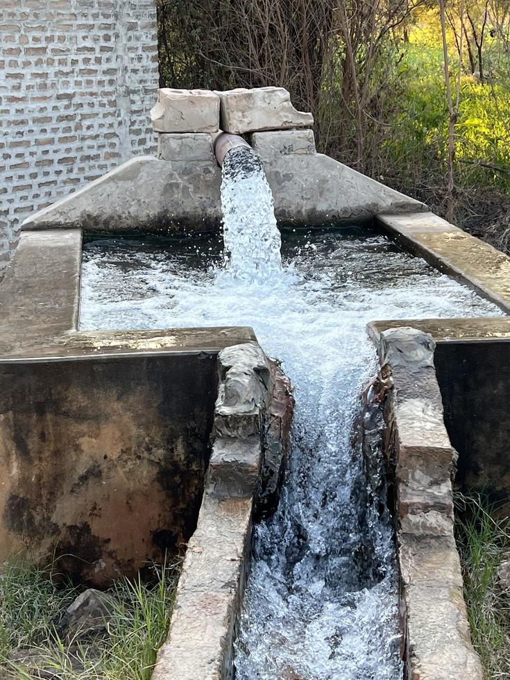 irrigatie water stromen van pijp naar kanaal voor landbouw velden foto