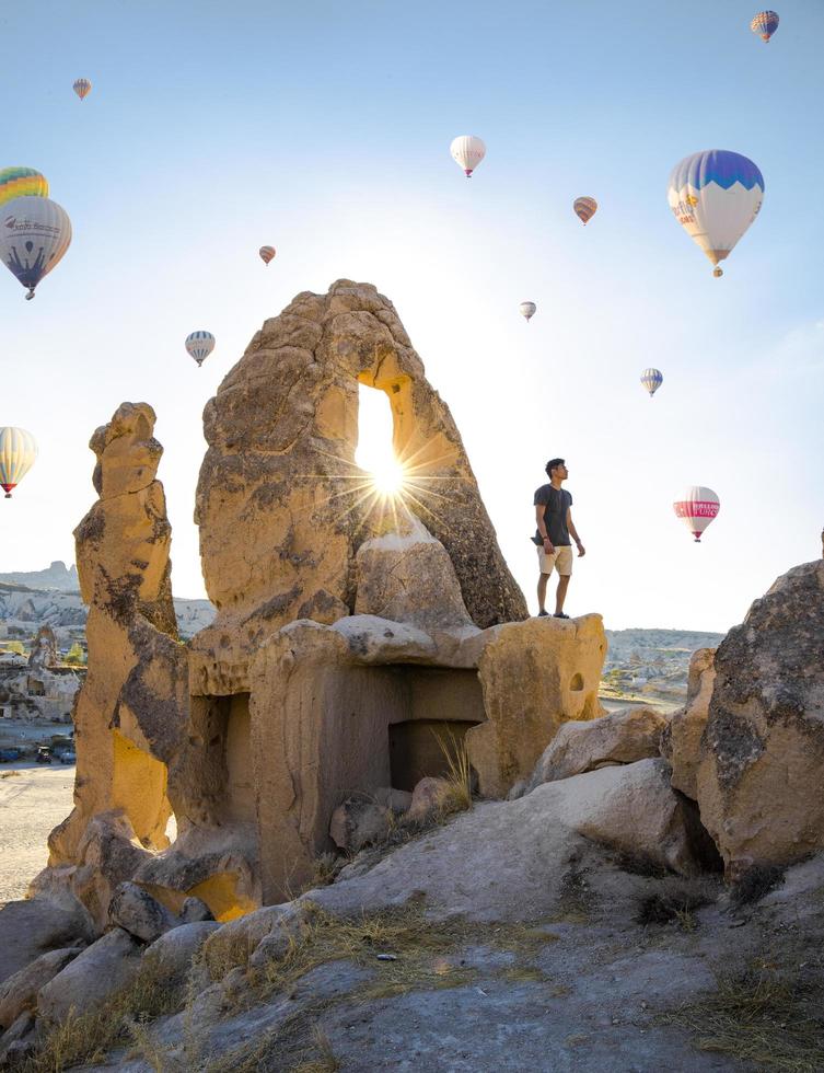 man staande op rotsachtige heuvel, luchtballonnen rond foto
