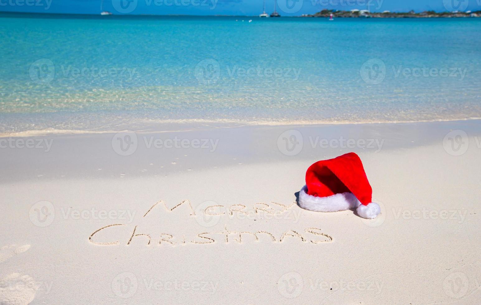 vrolijk Kerstmis geschreven Aan tropisch strand wit zand met Kerstmis hoed foto