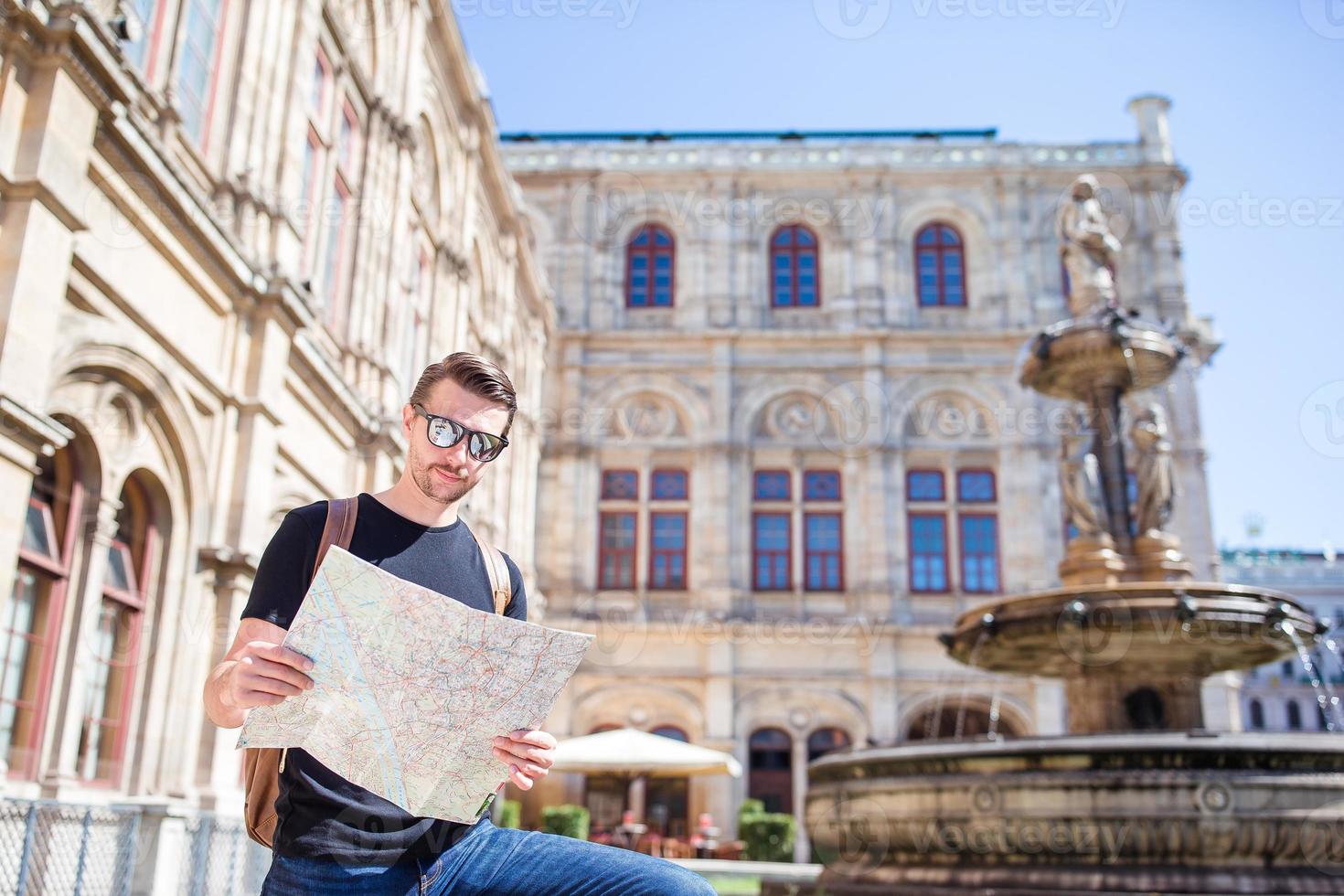 Mens toerist met een stad kaart en rugzak in Europa straat. Kaukasisch jongen op zoek met kaart van Europese stad. foto