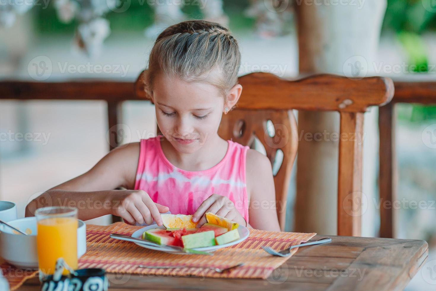 schattig klein meisje aan het ontbijt op terras foto