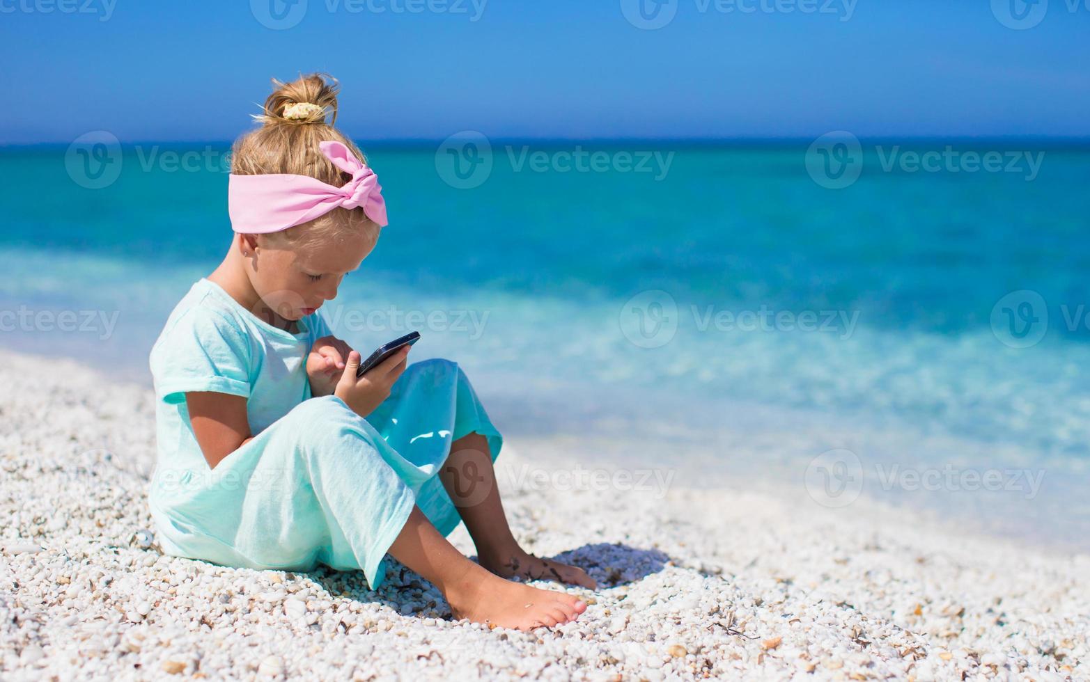 weinig schattig meisje nemen afbeeldingen Aan telefoon Bij tropisch strand foto