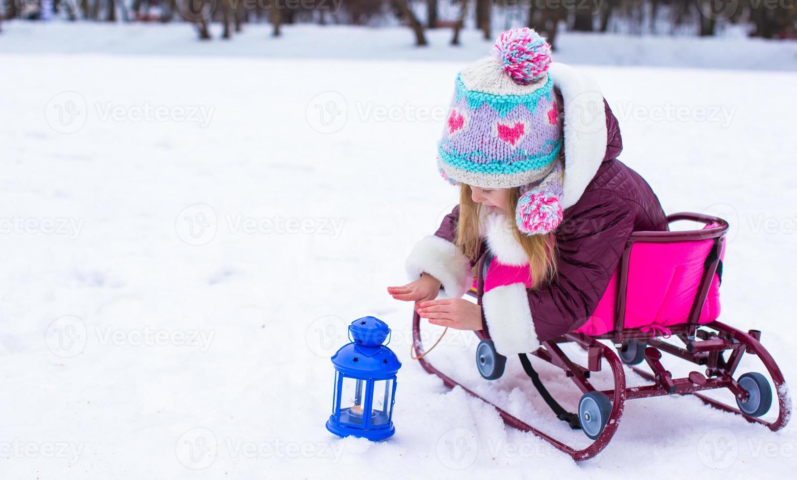 weinig meisje verwarmt haar handen Aan kaars in de lantaarn buitenshuis foto