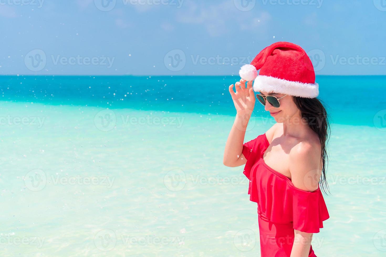 jong gelukkig vrouw in de kerstman hoed in zwempak Aan wit strand Aan Kerstmis vakantie foto