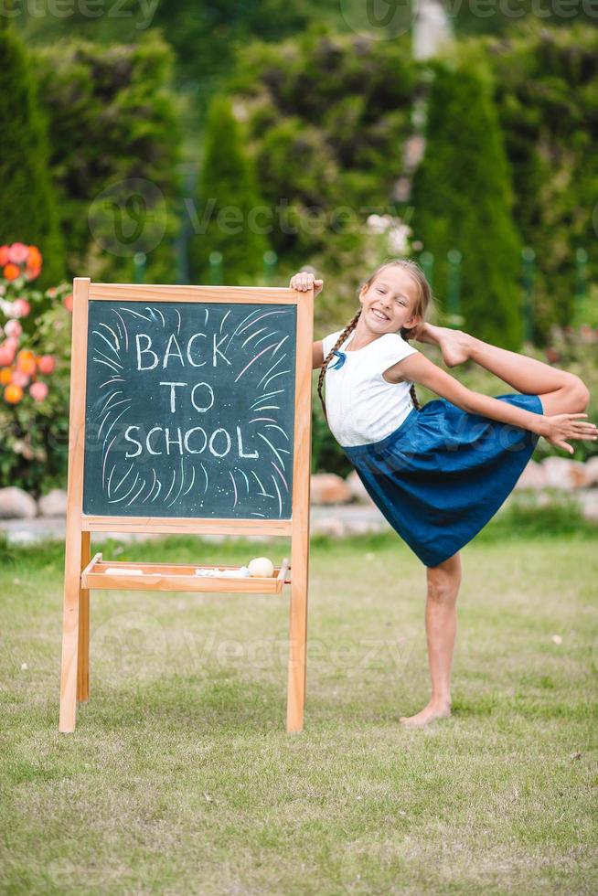 gelukkig weinig schoolmeisje met een schoolbord buitenshuis foto