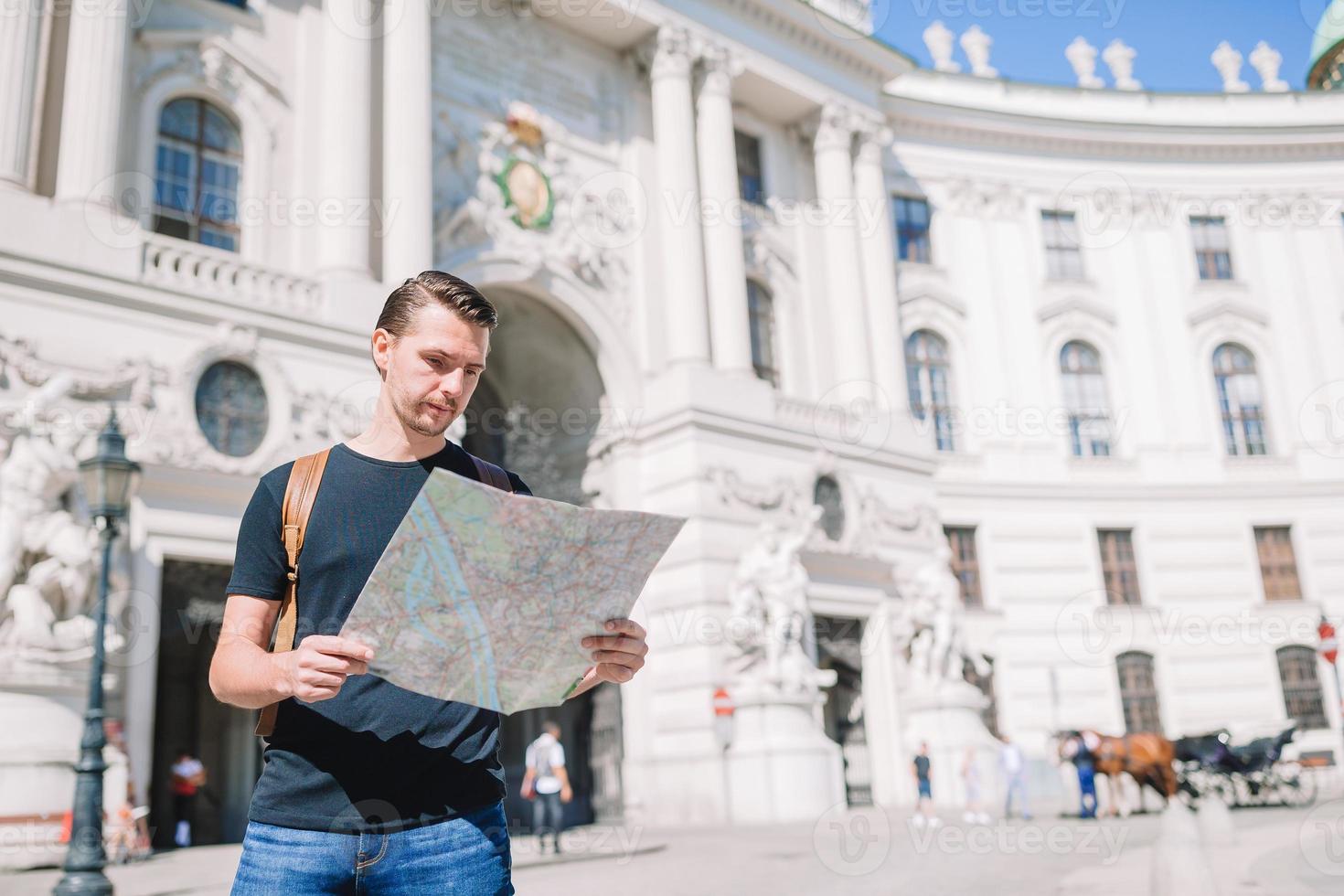 Mens toerist met een stad kaart en rugzak in Europa straat. Kaukasisch jongen op zoek met kaart van Europese stad. foto