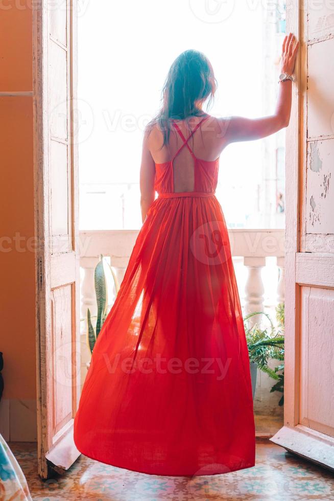 jong aantrekkelijk vrouw in rood jurk Aan oud balkon in appartement in Havana foto