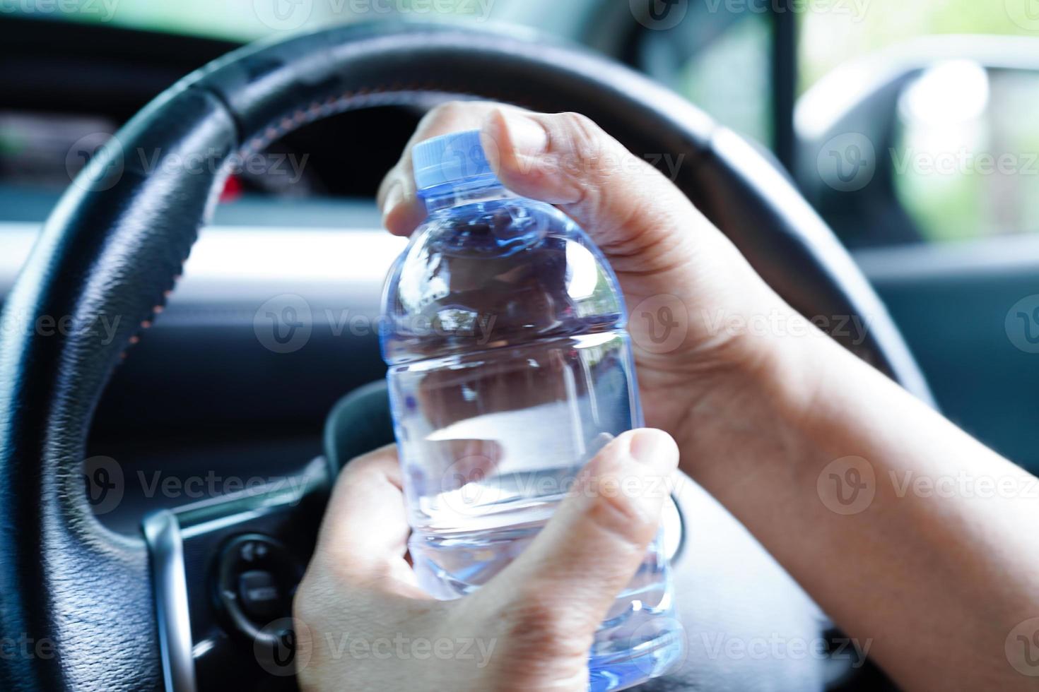 Aziatisch vrouw bestuurder houden verkoudheid water voor drinken in auto, gevaarlijk en risico een ongeluk. foto
