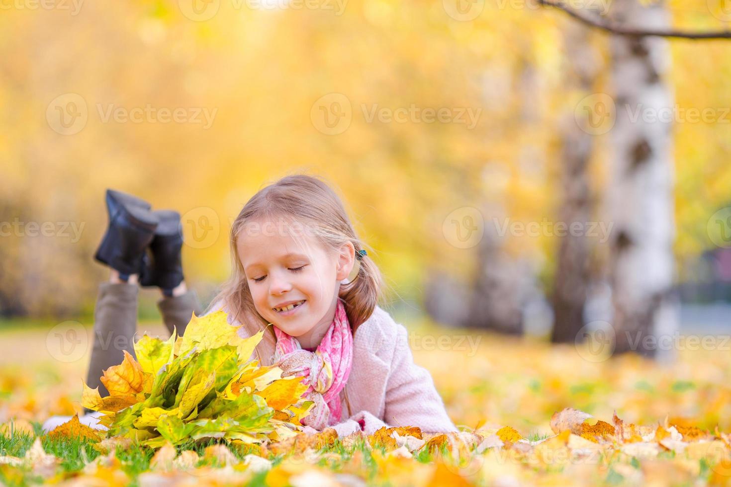 portret van aanbiddelijk weinig meisje met geel bladeren boeket in val. mooi glimlachen kind aan het liegen Aan bladeren tapijt foto
