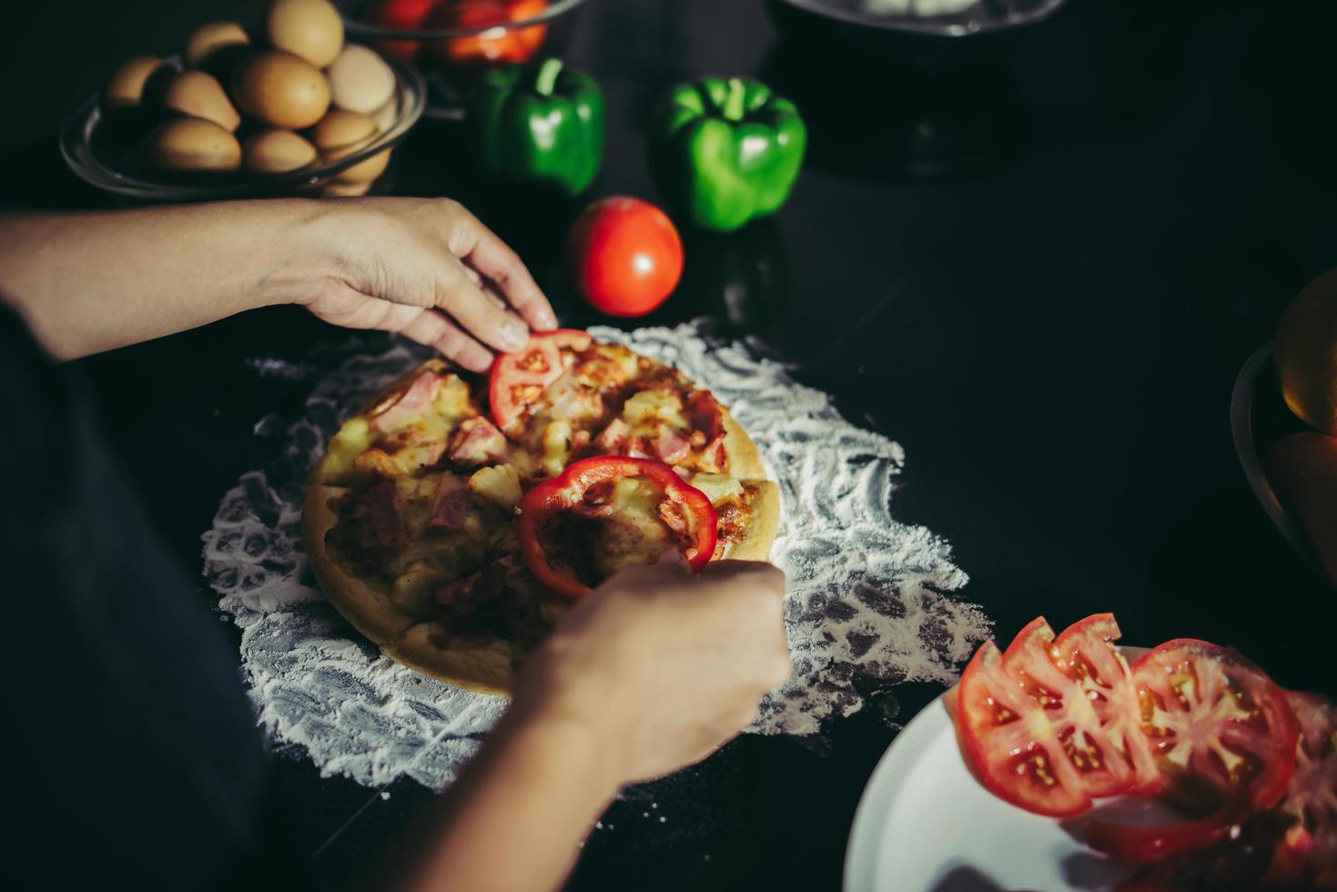 close-up van een vrouw toppings op zelfgemaakte pizza te zetten foto