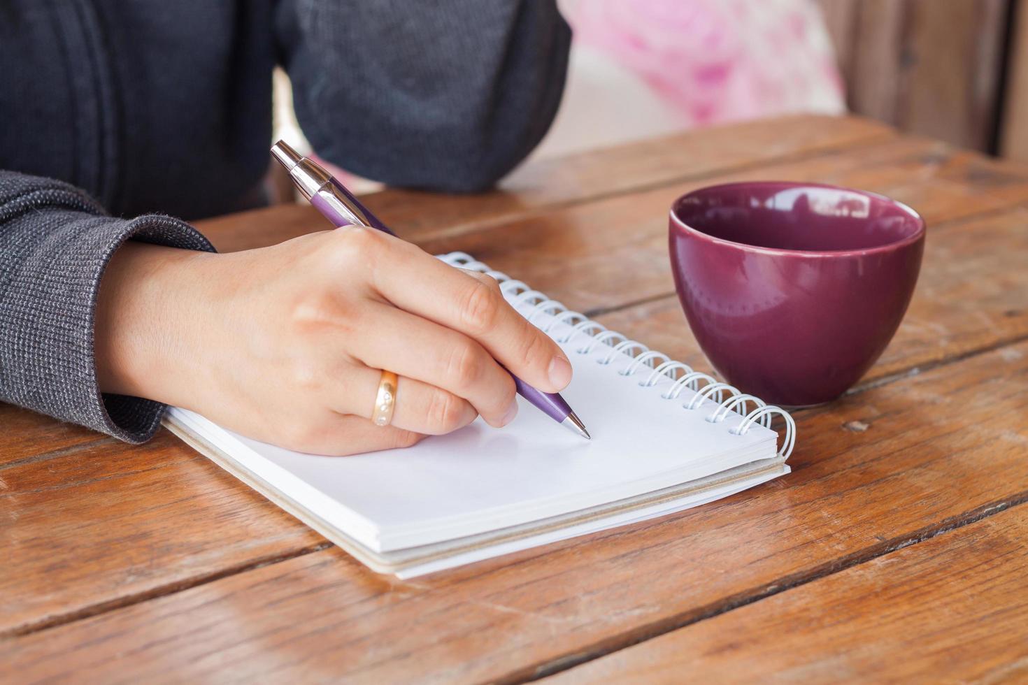 persoon die in een notitieboekje met een kopje koffie schrijft foto