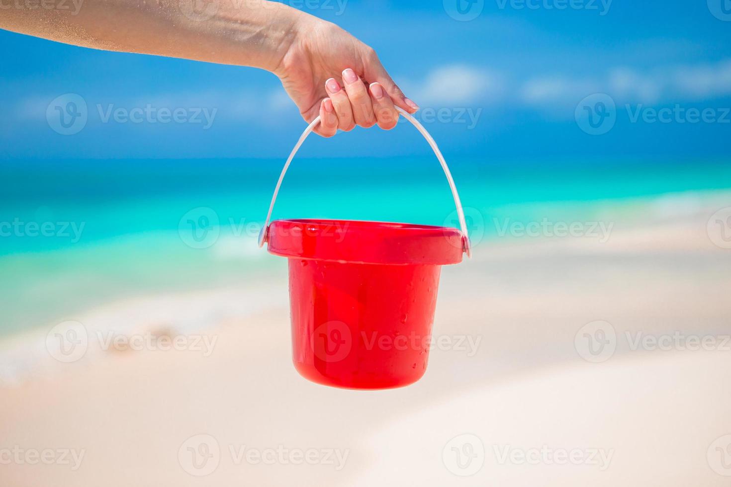 dichtbij omhoog hand- Holding een klein rood emmer Aan tropisch strand foto