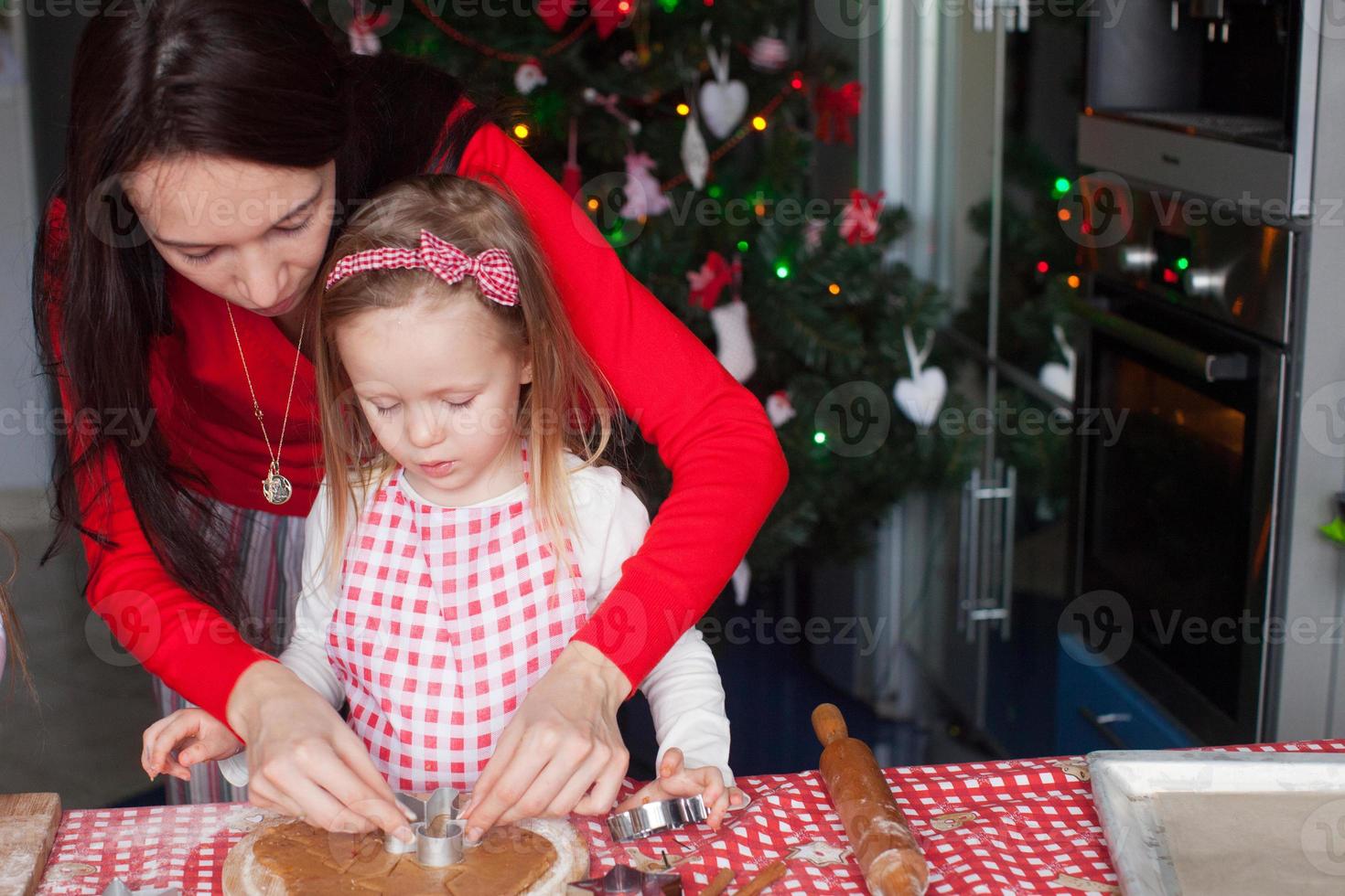 weinig aanbiddelijk meisje en jong moeder bakken Kerstmis peperkoek koekjes foto