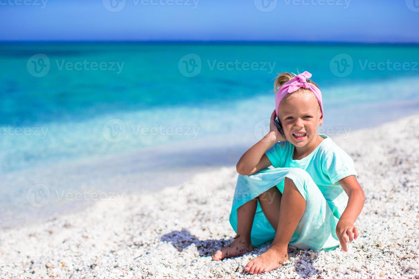 weinig aanbiddelijk meisje met cel telefoon gedurende strand vakantie foto