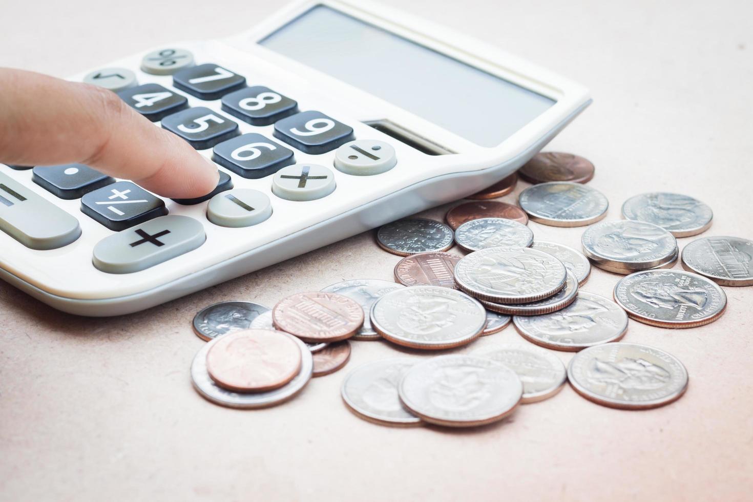 close-up van een hand op een rekenmachine met munten foto