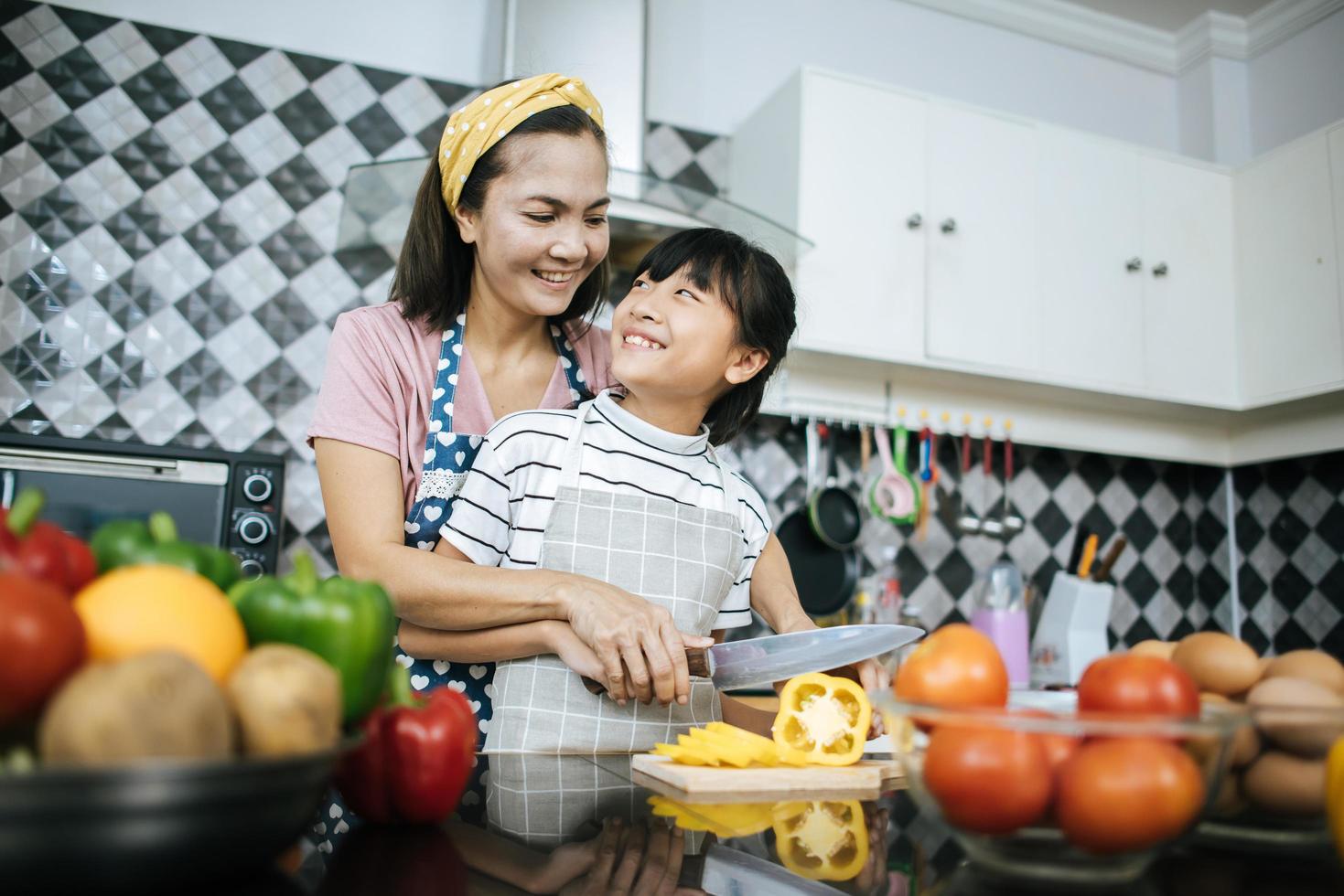 gelukkige moeder en dochter bereiden en hakken van groenten in de keuken foto