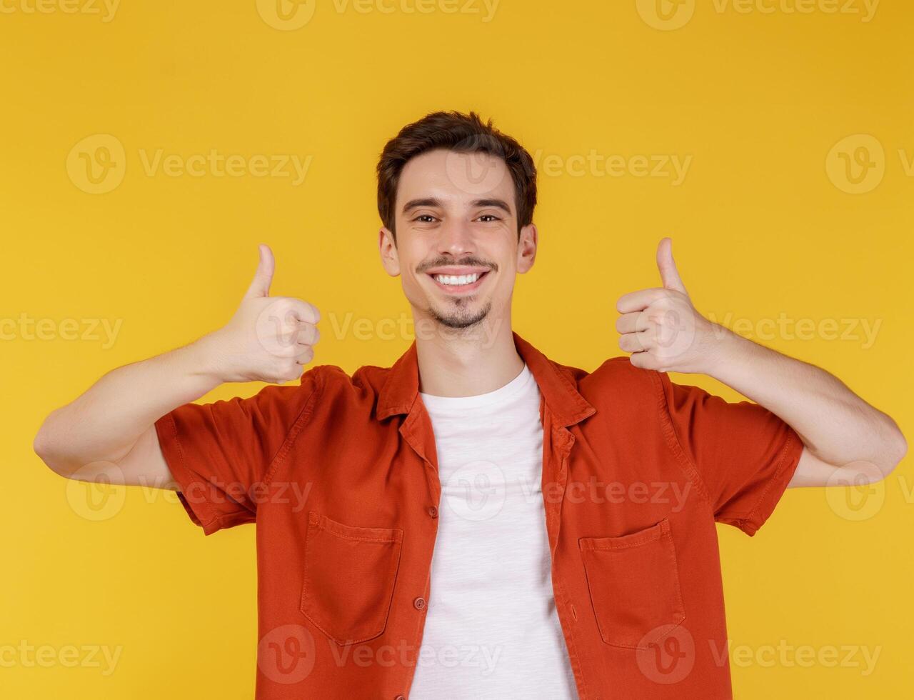 portret van gelukkig glimlachen jong Mens tonen duimen omhoog gebaar en op zoek Bij camera Aan geïsoleerd over- geel achtergrond foto