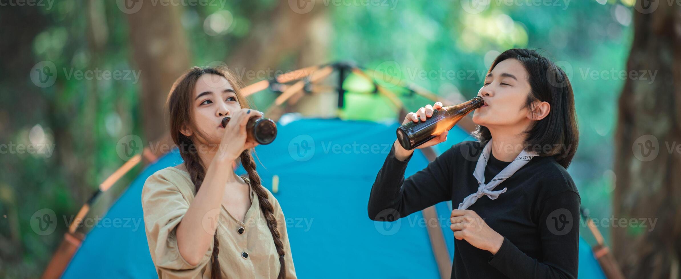 jong Dames juichen en drinken drank voorkant van camping tent foto