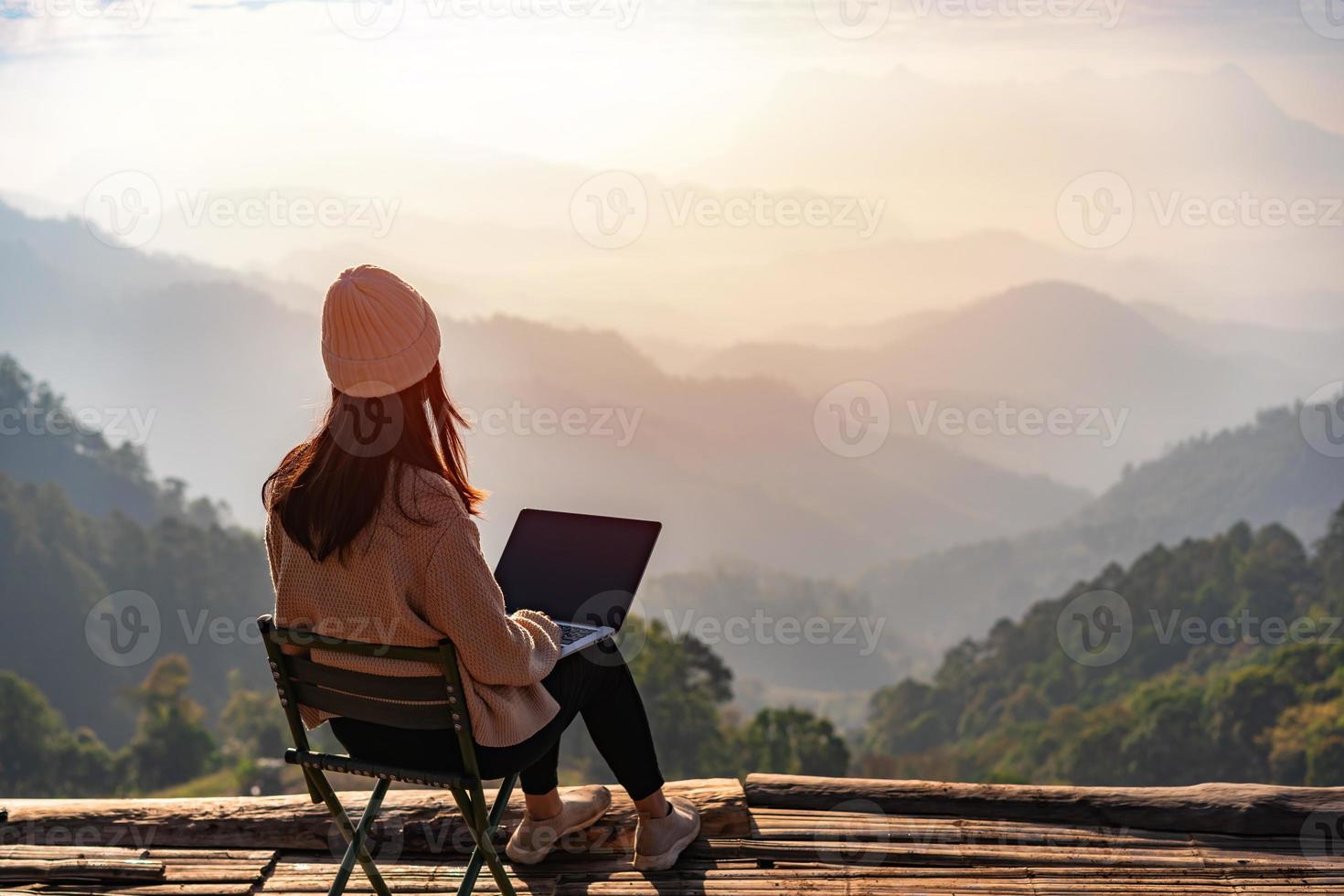 jonge vrouwelijke freelancer-reiziger die online werkt met behulp van laptop en geniet van het prachtige natuurlandschap met uitzicht op de bergen bij zonsopgang foto