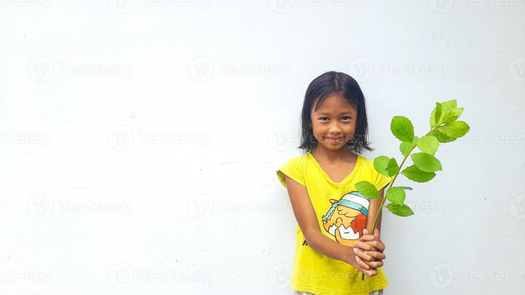 weinig meisje Holding jong fabriek. groen bladeren. ecologie concept. licht kleur achtergrond. foto