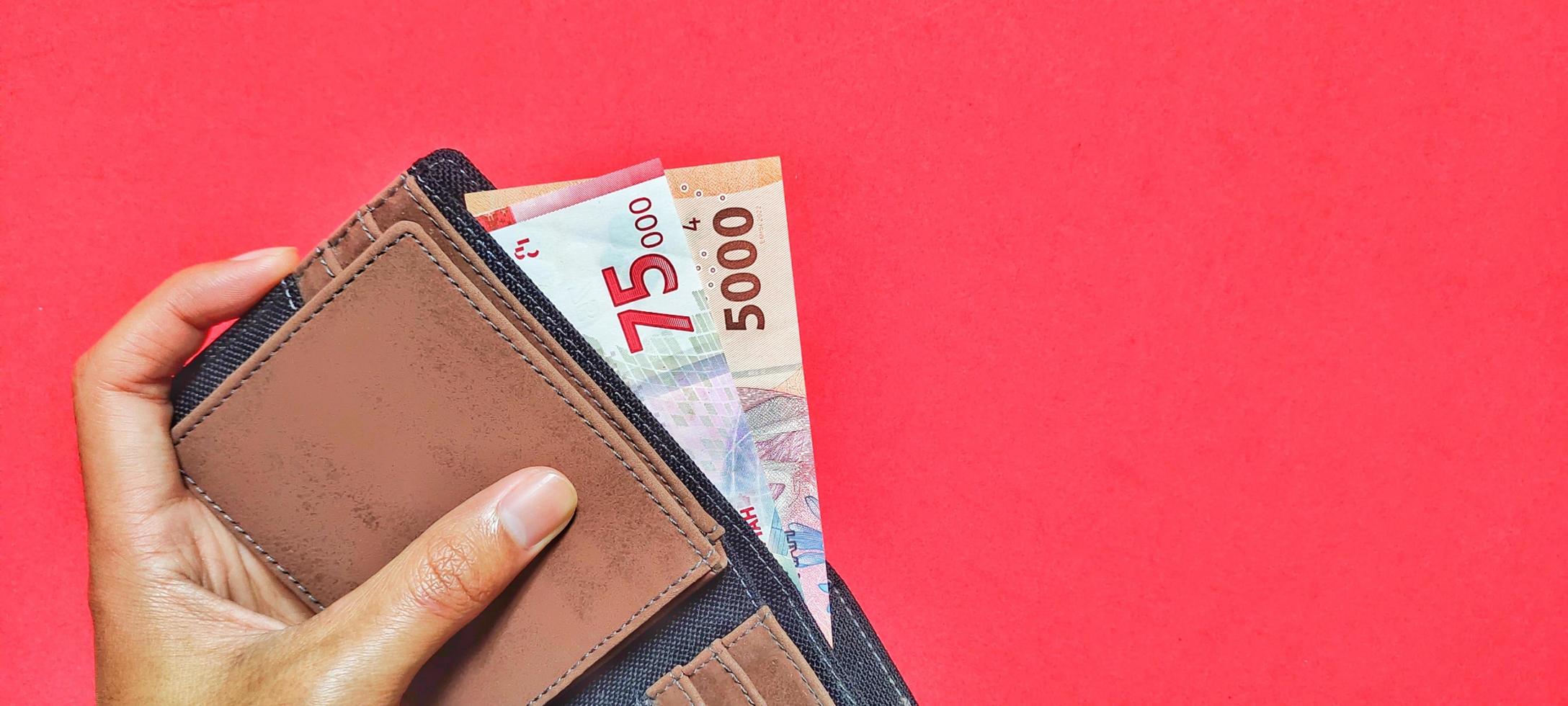 Mens Holding Indonesisch roepia bankbiljetten nieuw emissie 2022 in een portemonnee geïsoleerd Aan een rood achtergrond foto