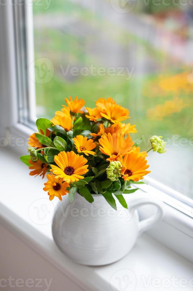 een boeket van helder calendula in een melk vaas staat Aan de vensterbank, helder herfst met een venster. foto