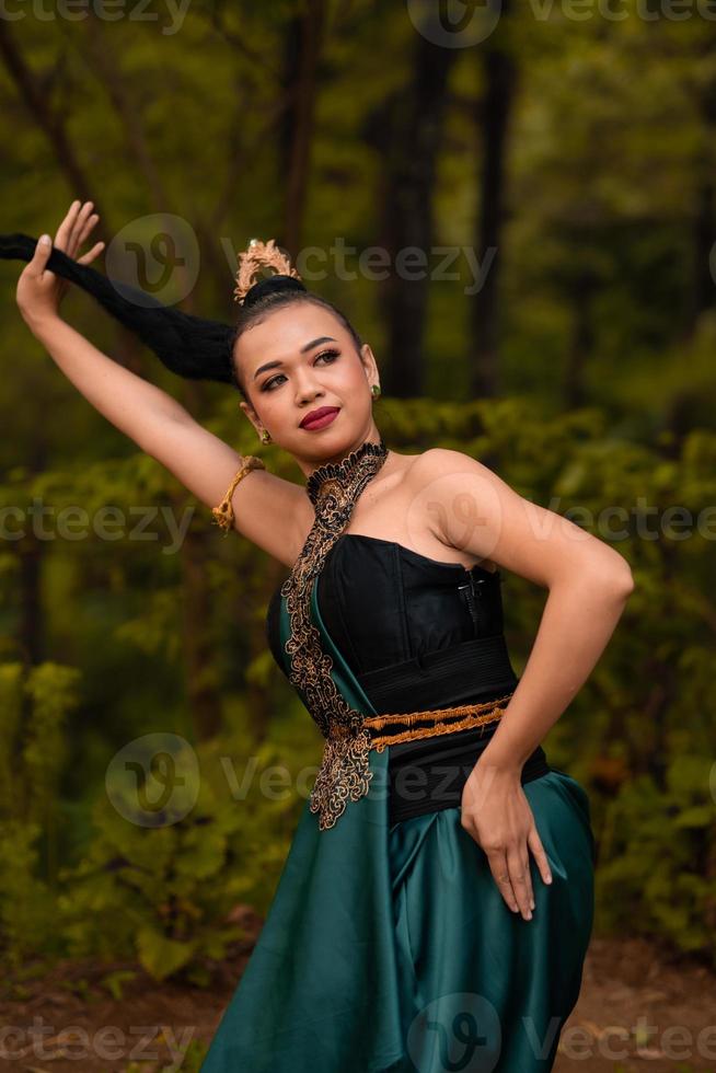 Aziatisch vrouw Holding haar zwart haar- in een groen kostuum terwijl vervelend bedenken en poseren in voorkant van de Woud gedurende de dans festival foto