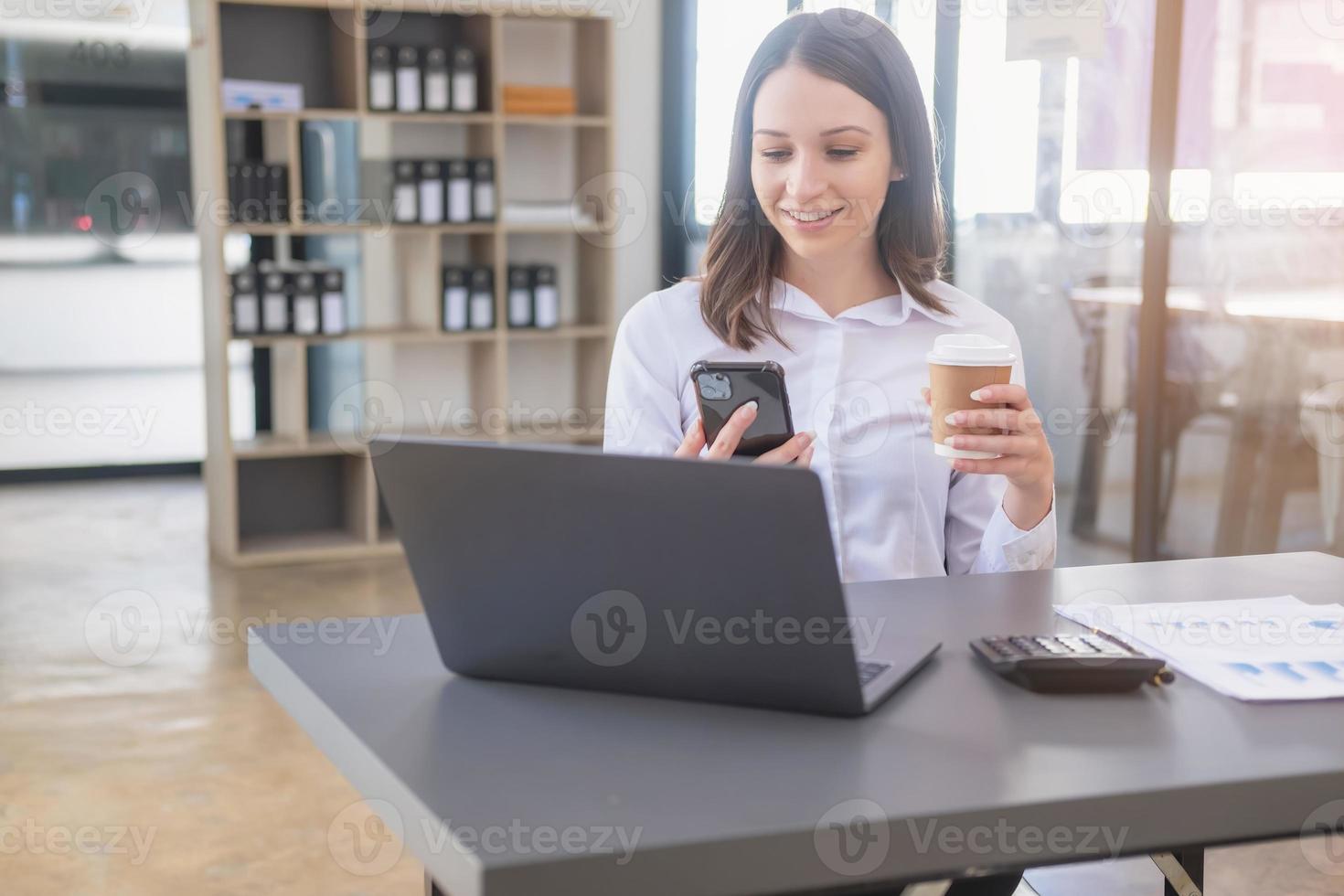 marketing, financiën, boekhouding, planning, wit biraciaal zakenvrouw gebruik makend van mobiel telefoon naar contact klanten informeren hen van bedrijf bedrijf partnerschappen Aan kantoor tafel met laptop en documenten. foto