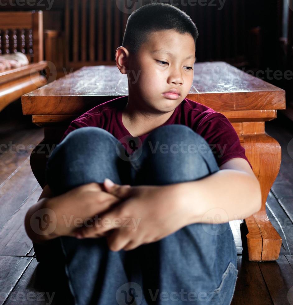 portret van een weinig Aziatisch jongen, kind verdrietig gezicht, ongelukkig kind zittend knuffel knieën Aan de vloer, emotie verdrietig en verdrietig gezicht, depressie kinderen concept foto