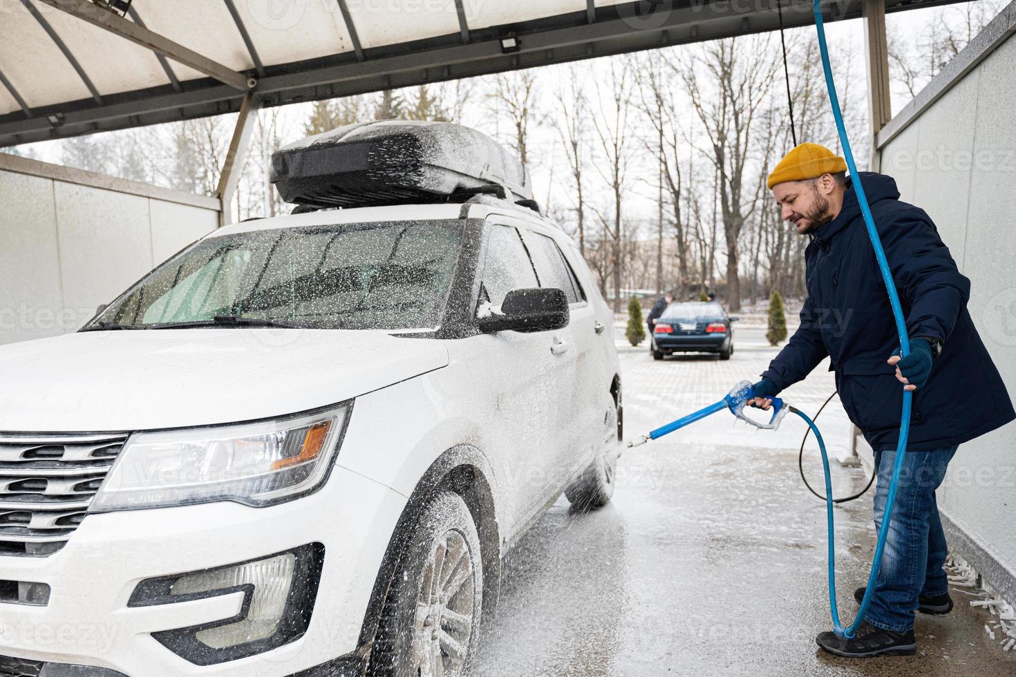 Mens het wassen Amerikaans suv auto met dak rek Bij een zelf onderhoud wassen in verkoudheid het weer. foto