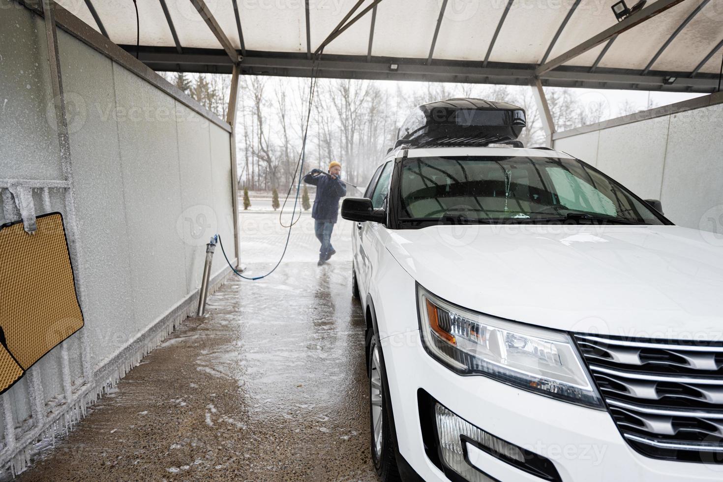 Mens het wassen hoog druk water Amerikaans suv auto met dak rek Bij zelf onderhoud wassen in verkoudheid het weer. foto
