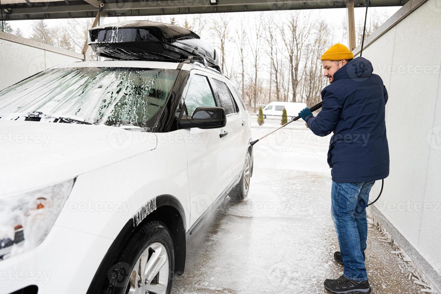 Mens het wassen hoog druk water Amerikaans suv auto met dak rek Bij zelf onderhoud wassen in verkoudheid het weer. foto