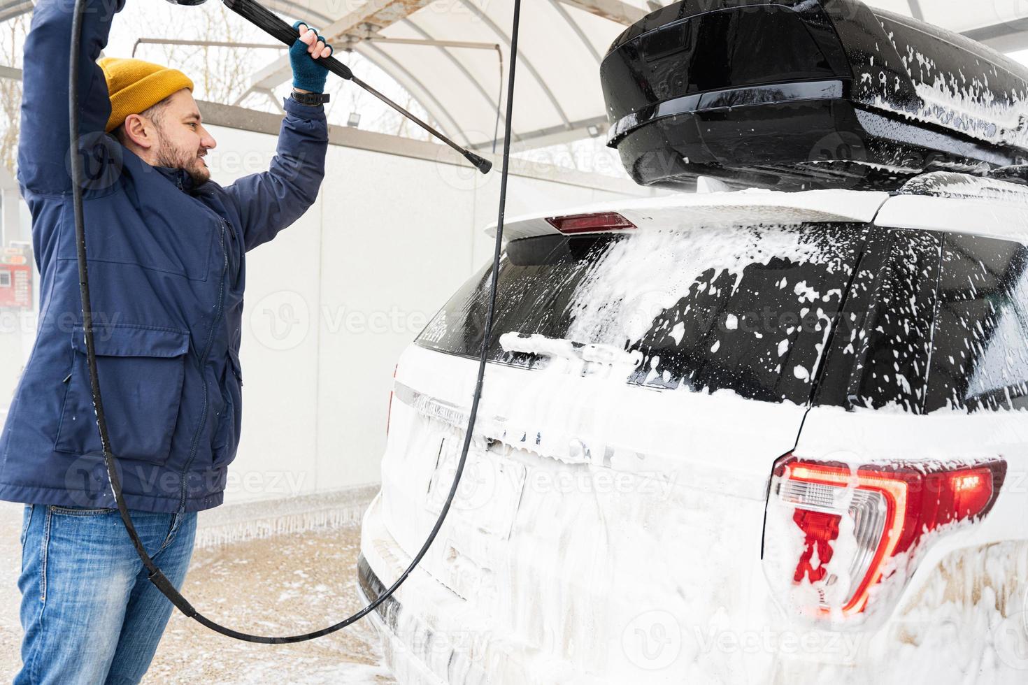 Mens het wassen hoog druk water Amerikaans suv auto met dak rek Bij zelf onderhoud wassen in verkoudheid het weer. foto