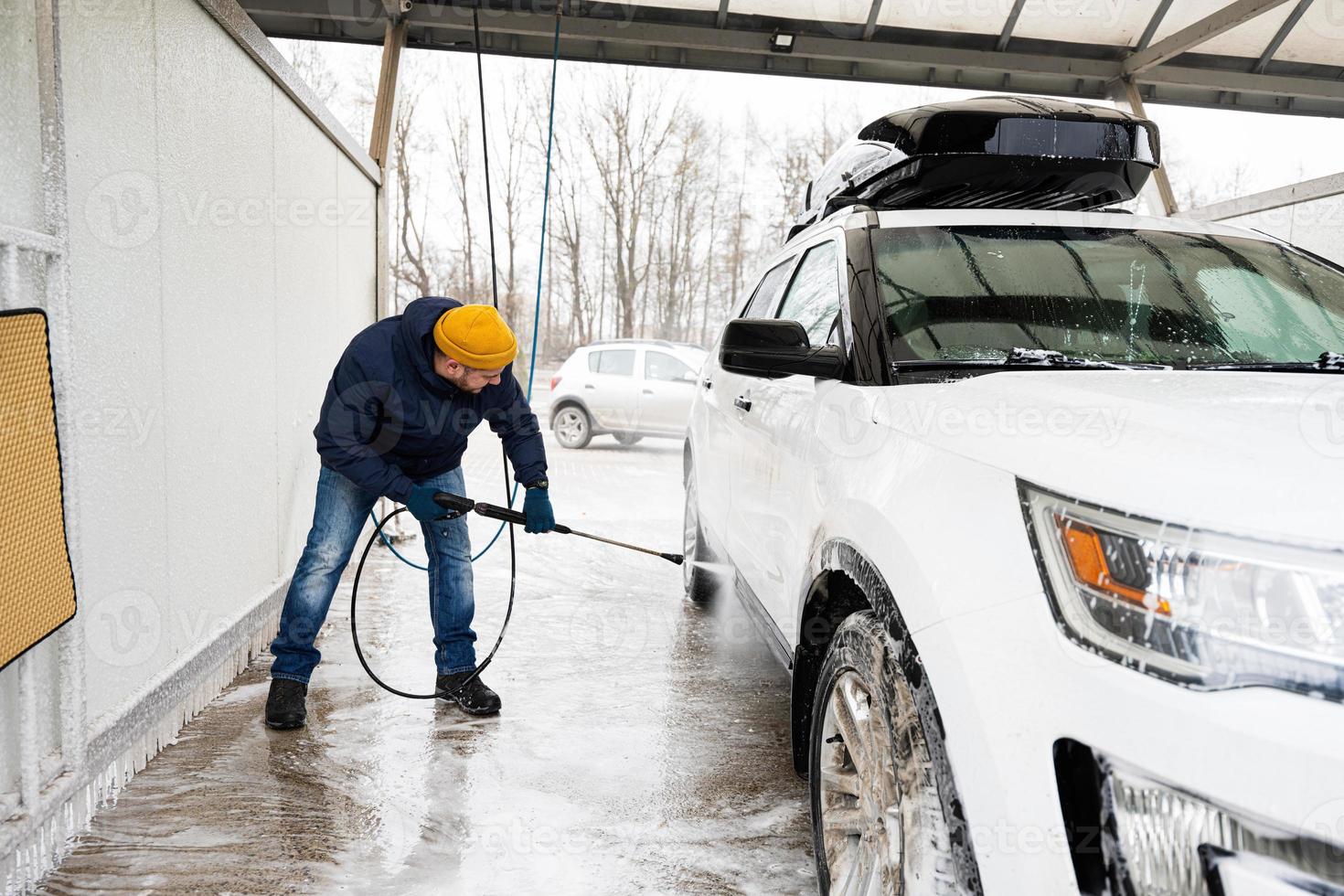 Mens het wassen hoog druk water Amerikaans suv auto met dak rek Bij zelf onderhoud wassen in verkoudheid het weer. foto