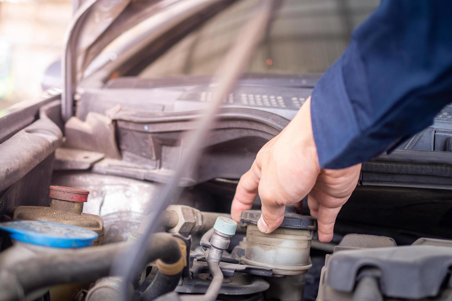 handen van jong professioneel monteur in uniform schrijven Aan klembord tegen auto in Open kap Bij de reparatie garage. onderhoud zie. auto onderhoud en onderhoud foto