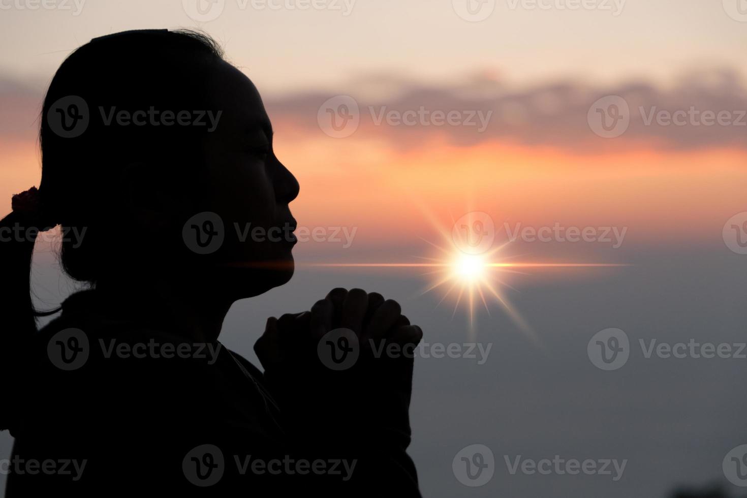 geloof van christen concept. geestelijk gebed handen over- zon schijnen met wazig mooi zonsondergang achtergrond. vrouw handen aanbidden god met liefde en vertrouwen. silhouet van een vrouw bidden met een kruis. foto