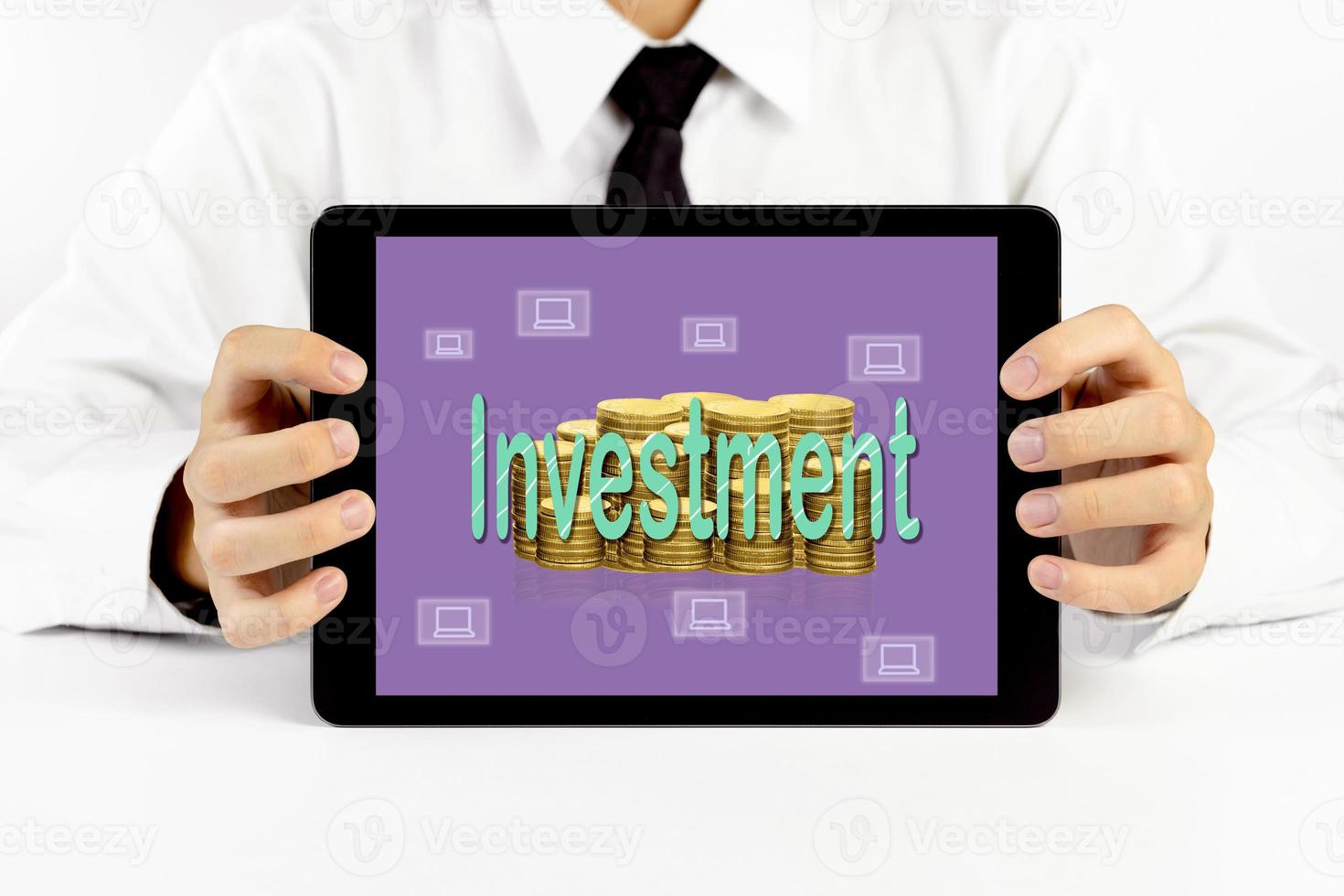 zakenman Holding een tablet met groen woord investering en gouden munten stapels en laptop pictogrammen foto