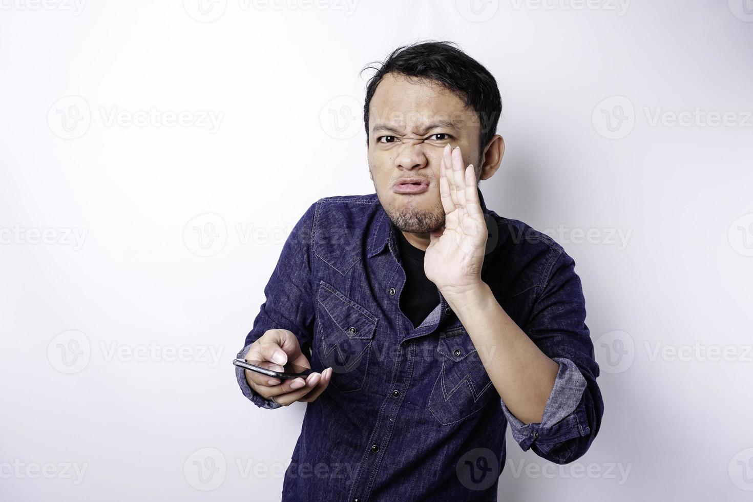 de boos en boos gezicht van Aziatisch Mens in blauw overhemd Holding zijn telefoon geïsoleerd wit achtergrond. foto