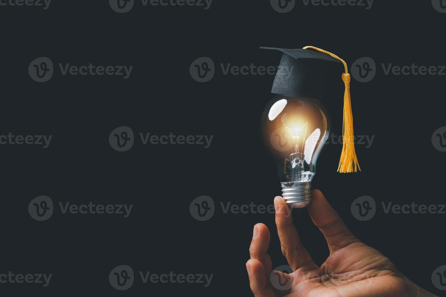 academie en succes afstuderen onderwijs concept. zakenman hand- Holding helder, elektrisch licht lamp met mate pet Aan zwart achtergrond. bedrijf opleiding, kennis, aan het leren idee met kopiëren ruimte. foto