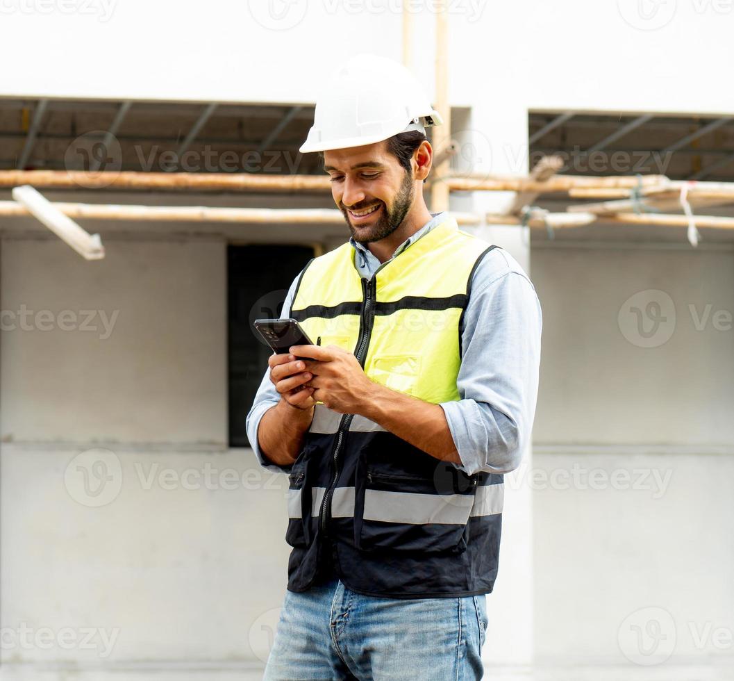 mannetje architect of ingenieur gebruik makend van mobiel telefoon voor communicatie terwijl werken Bij bouw plaats. professioneel gebouw aannemer staand Bij behuizing ontwikkeling plaats toepassingen smartphone Aan de functie. foto