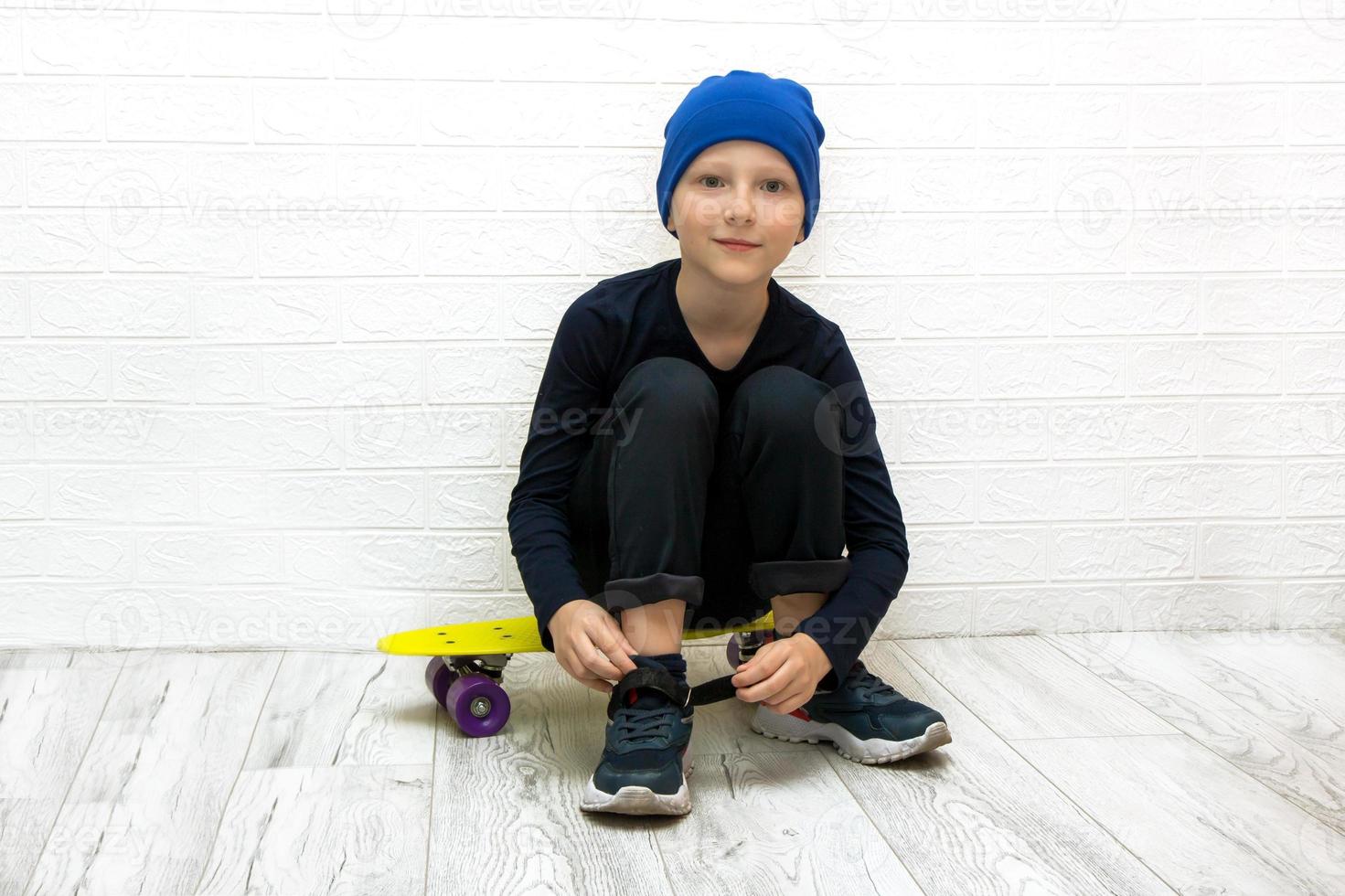 jongen in een hoed ritsen omhoog zijn sportschoenen terwijl zittend Aan een skateboard in neon licht foto