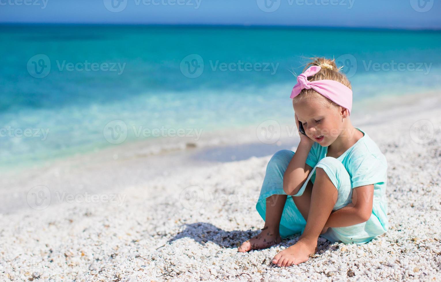 weinig aanbiddelijk meisje pratend Bij telefoon gedurende strand vakantie foto