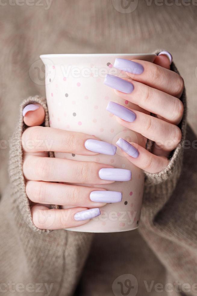 meisjes handen met delicaat Purper manicure Holding een kop van thee. foto